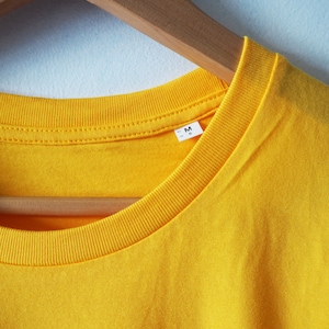 May include: A yellow t-shirt with a size tag that says "M" hanging on a wooden hanger.