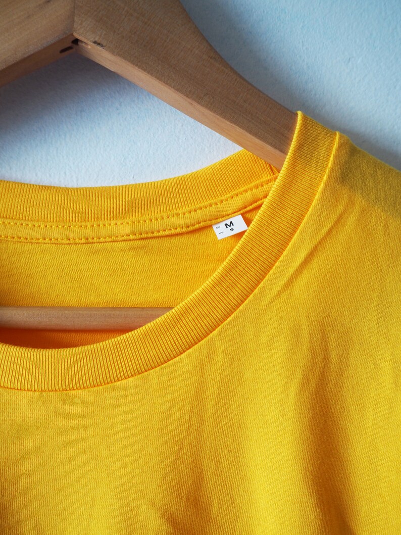 May include: A yellow t-shirt with a size tag that says "M" hanging on a wooden hanger.