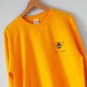 May include: A yellow sweatshirt with a black bee graphic and the text "BEE KIND." printed on the front.