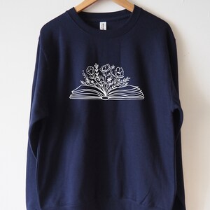 May include: A navy blue sweatshirt with a white graphic of an open book with flowers growing out of it.