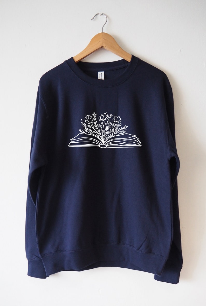 May include: A navy blue sweatshirt with a white graphic of an open book with flowers growing out of it.
