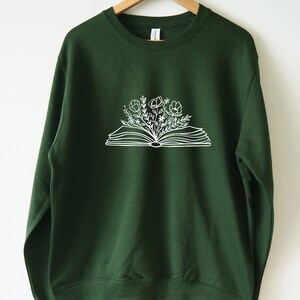 May include: A dark green sweatshirt with a white outline of an open book with flowers growing out of it.