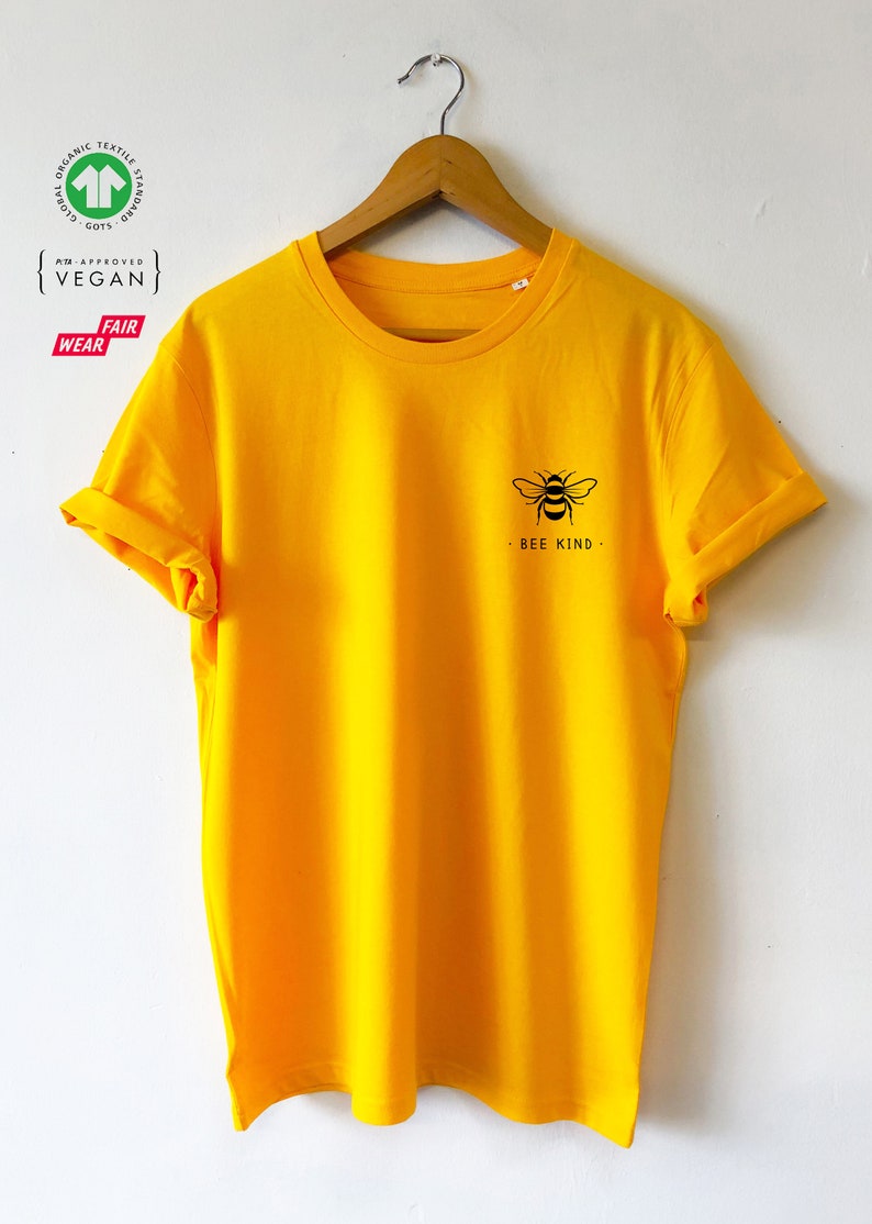 May include: A yellow t-shirt with a black bee graphic and the text "Bee Kind" on the front. The shirt is made of organic cotton and is certified vegan and fair trade.