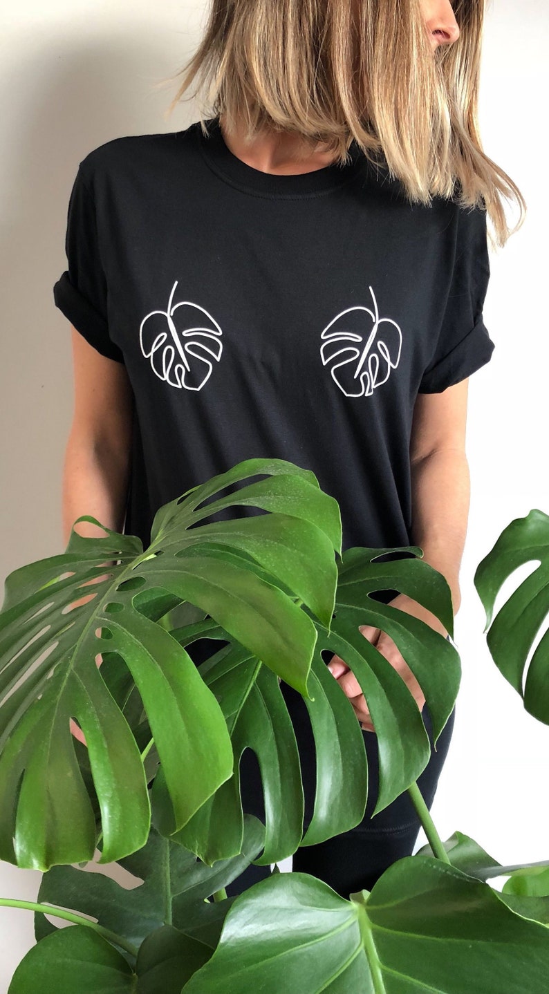 May include: A black t-shirt with a white outline of two monstera leaves on the front.