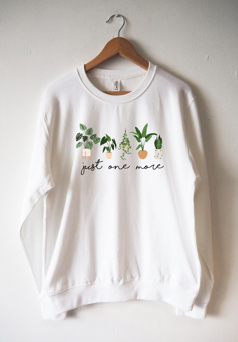 Puede incluir: Sudadera blanca con un gr&aacute;fico de plantas en maceta y el texto "just one more".