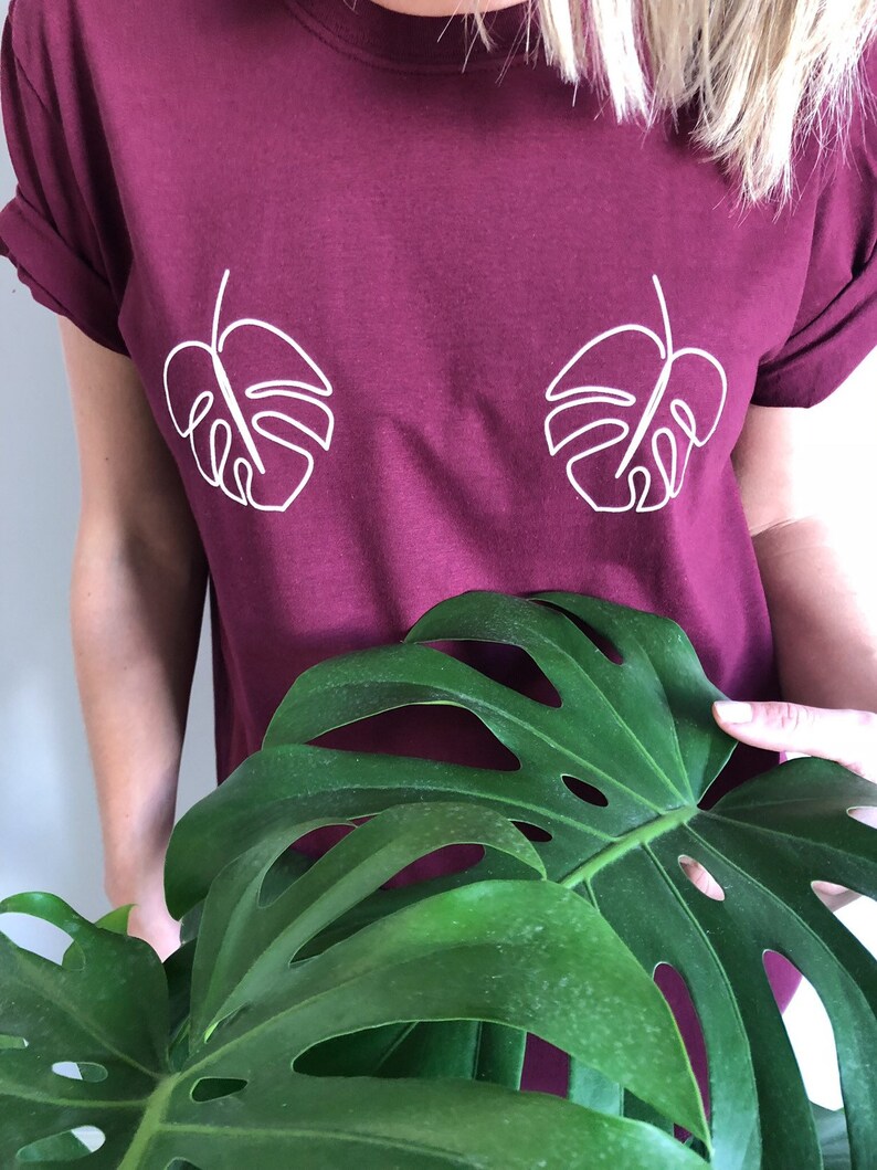 May include: A maroon t-shirt with a white outline of two monstera leaves on the front.