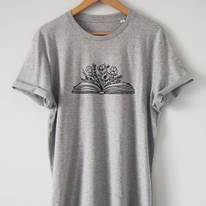 May include: A gray t-shirt with a black and white graphic of an open book with flowers growing out of it.