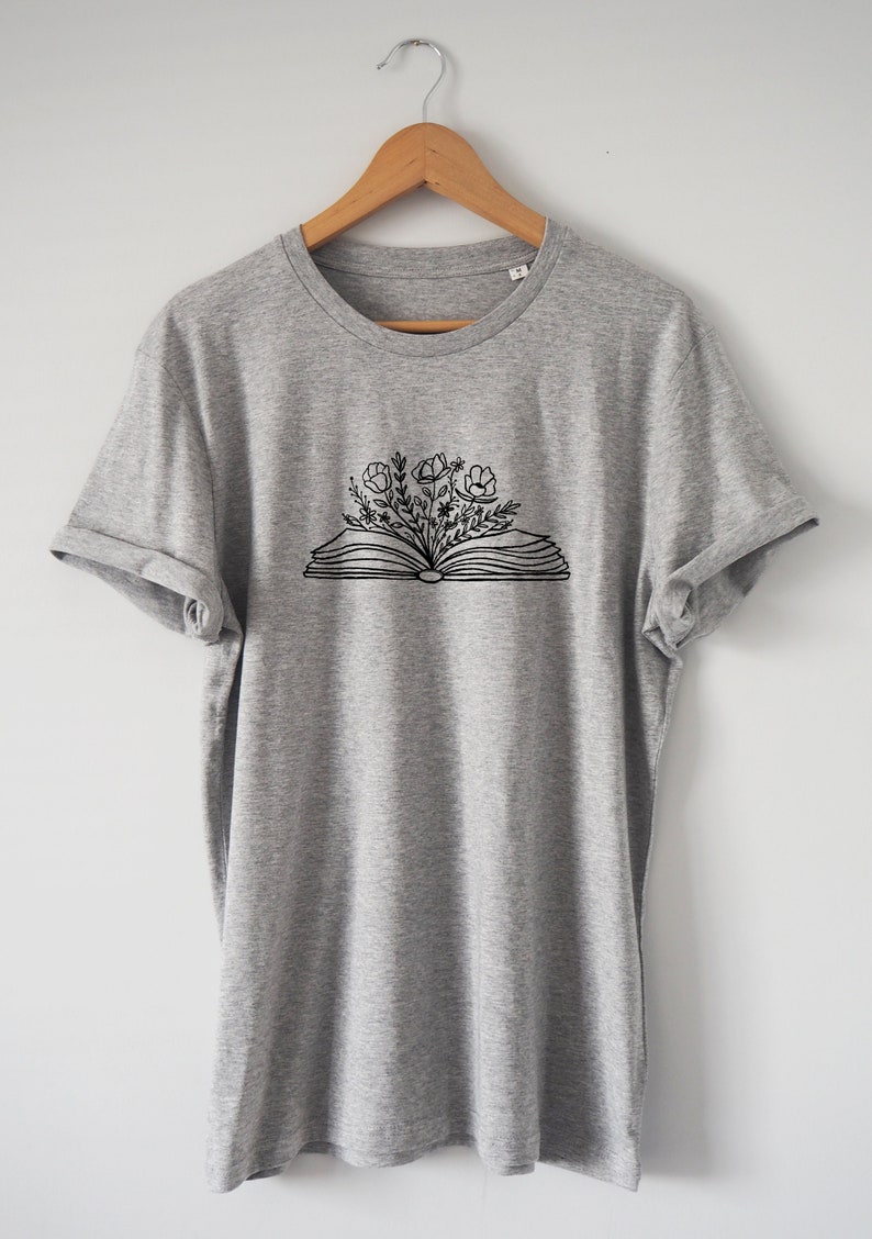 May include: A gray t-shirt with a black and white graphic of an open book with flowers growing out of it.
