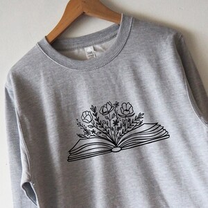 May include: A gray sweatshirt with a black line drawing of an open book with flowers growing out of it.