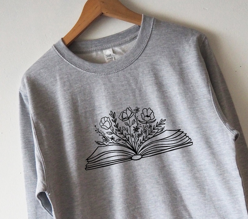 May include: A gray sweatshirt with a black line drawing of an open book with flowers growing out of it.