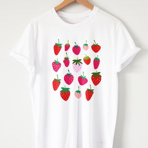 Puede incluir: Camiseta blanca con estampado gr&aacute;fico de fresas rojas y rosas.