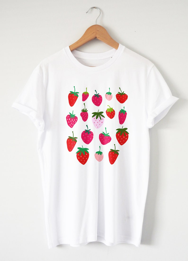 Puede incluir: Camiseta blanca con estampado gr&aacute;fico de fresas rojas y rosas.