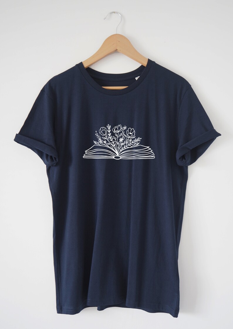 May include: A navy blue t-shirt with a white graphic of an open book with flowers growing out of it.