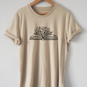 May include: A beige t-shirt with a black graphic of an open book with flowers growing out of it.
