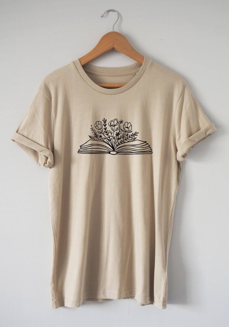May include: A beige t-shirt with a black graphic of an open book with flowers growing out of it.