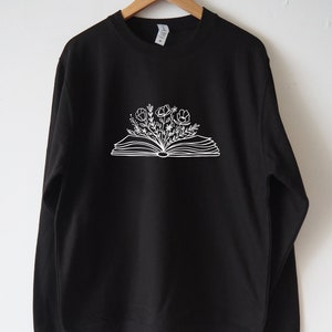 May include: Black sweatshirt with a white outline of an open book with flowers growing out of it.