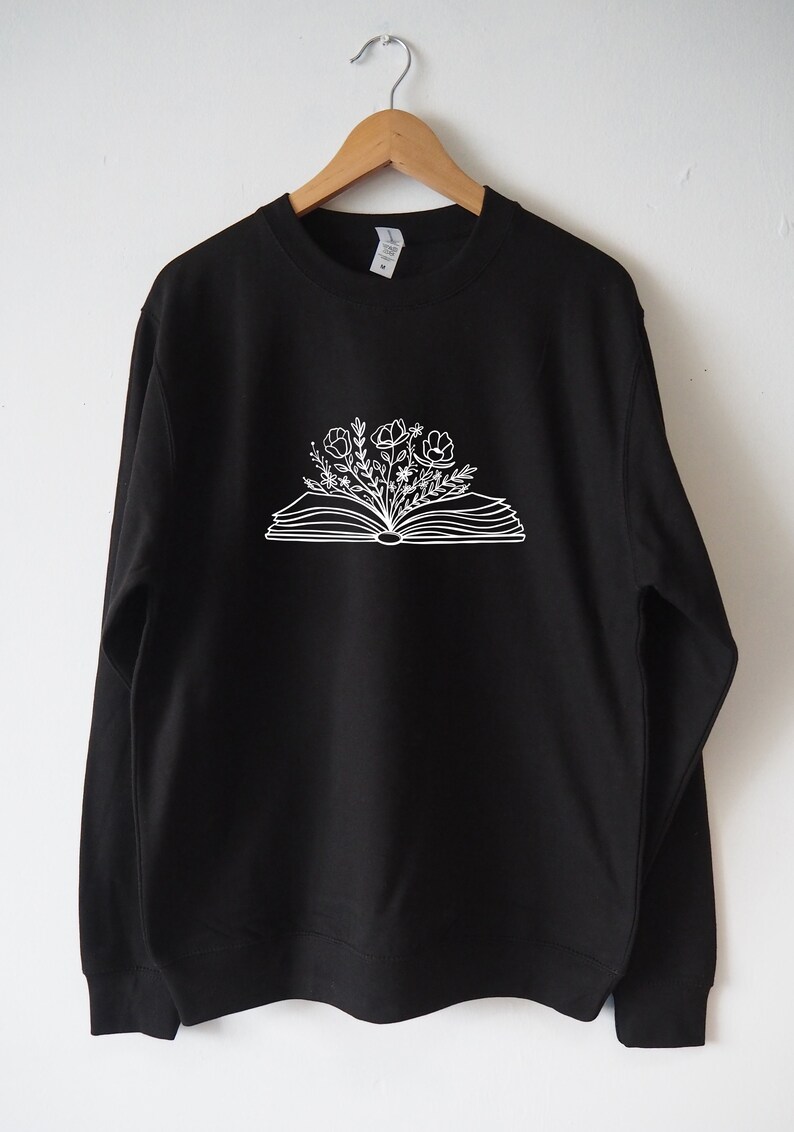 May include: Black sweatshirt with a white outline of an open book with flowers growing out of it.