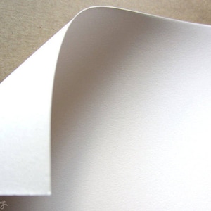 May include: A close-up of a white sheet of paper with a slightly textured surface. The paper is folded over at the top, creating a curved edge.