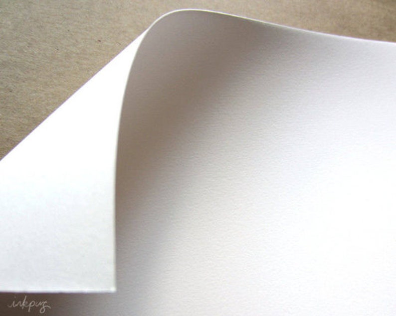 May include: A close-up of a white sheet of paper with a slightly textured surface. The paper is folded over at the top, creating a curved edge.