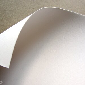 May include: Close-up of a white sheet of paper with a textured surface. The paper is folded over at the top, creating a curved edge.