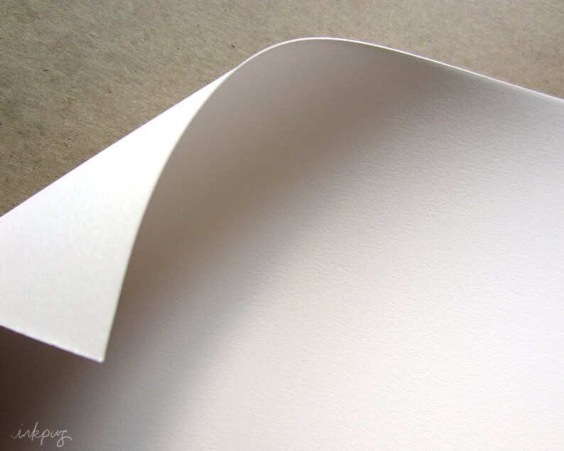 May include: Close-up of a white sheet of paper with a textured surface. The paper is folded over at the top, creating a curved edge.
