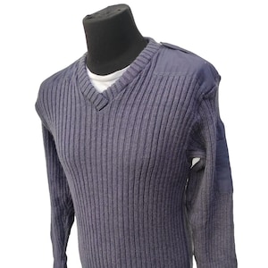 May include: A navy blue ribbed knit sweater with a V-neck and reinforced shoulder patches. The long-sleeved sweater is displayed on a mannequin. The sweater has a classic design.