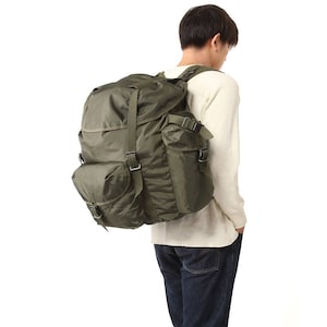 May include: Olive green backpack with multiple pockets and adjustable straps. The backpack has a large main compartment and two side pockets, ideal for outdoor activities or travel. The bag is made of a durable, water-resistant material.