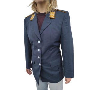 Puede incluir: Blazer azul marino con botones blancos y dos bolsillos delanteros. El blazer tiene charreteras doradas y amarillas. La chaqueta es de estilo militar vintage.