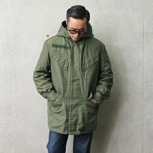 Puede incluir: Chaqueta con capucha verde oliva con múltiples bolsillos y un cordón. La chaqueta tiene un corte relajado y se combina con vaqueros azules. La chaqueta cuenta con cierre de cremallera frontal y capucha.