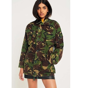 Puede incluir: Chaqueta de camuflaje en tonos verdes, marrones y beige. La chaqueta tiene múltiples bolsillos, cierre de botones en la parte delantera y cuello. Es una chaqueta de estilo militar.