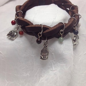 May include: A brown leather bracelet with multiple charms, including a Buddha head, beads, and a small elephant. The bracelet has a magnetic clasp.