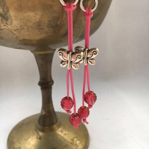 Pode incluir: Brincos de argola rosa e prata com pingentes de borboleta e contas de vidro rosa.