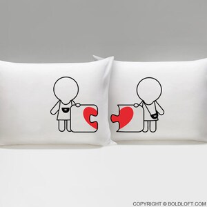 May include: Two white pillowcases with black line drawings of people holding puzzle pieces shaped like hearts. The hearts are red. The text "COPYRIGHT &copy; BOLDLOFT.COM" is at the bottom of the image.