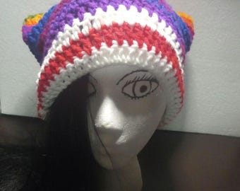 May include: A colorful, handmade crochet hat. The hat features horizontal stripes of purple, white, red, and blue. The hat is displayed on a mannequin head with black hair.