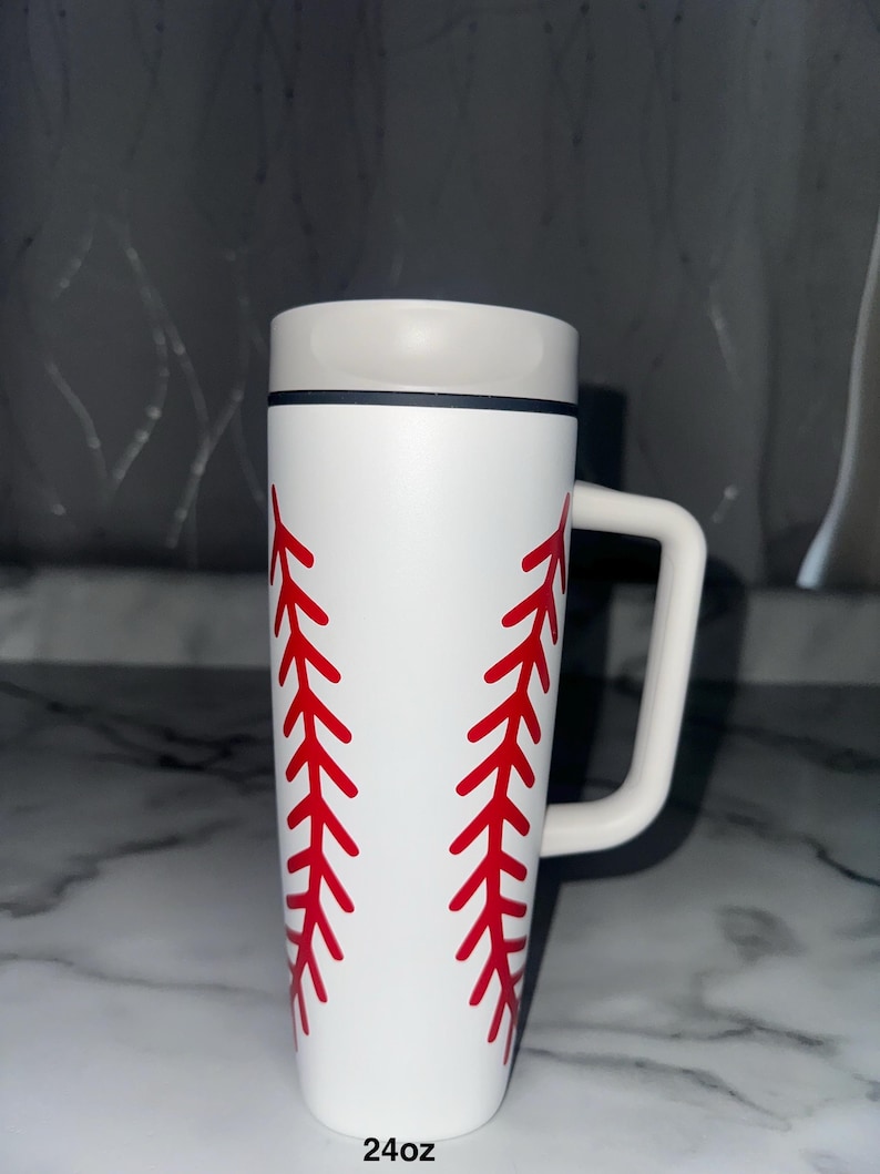 Puede incluir: Taza blanca con tem&aacute;tica de b&eacute;isbol con detalles de costuras rojas. La taza tiene un asa blanca y un borde gris. El texto "24oz" est&aacute; impreso en la parte inferior de la taza. Ideal para los fan&aacute;ticos del b&eacute;isbol.