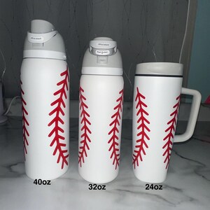 Puede incluir: Tres botellas de agua blancas y una taza con dise&ntilde;os de costuras de b&eacute;isbol rojas. Las botellas est&aacute;n etiquetadas como 40oz y 32oz, y la taza est&aacute; etiquetada como 24oz. Las botellas tienen tapas grises y la taza tiene un borde y asa grises.