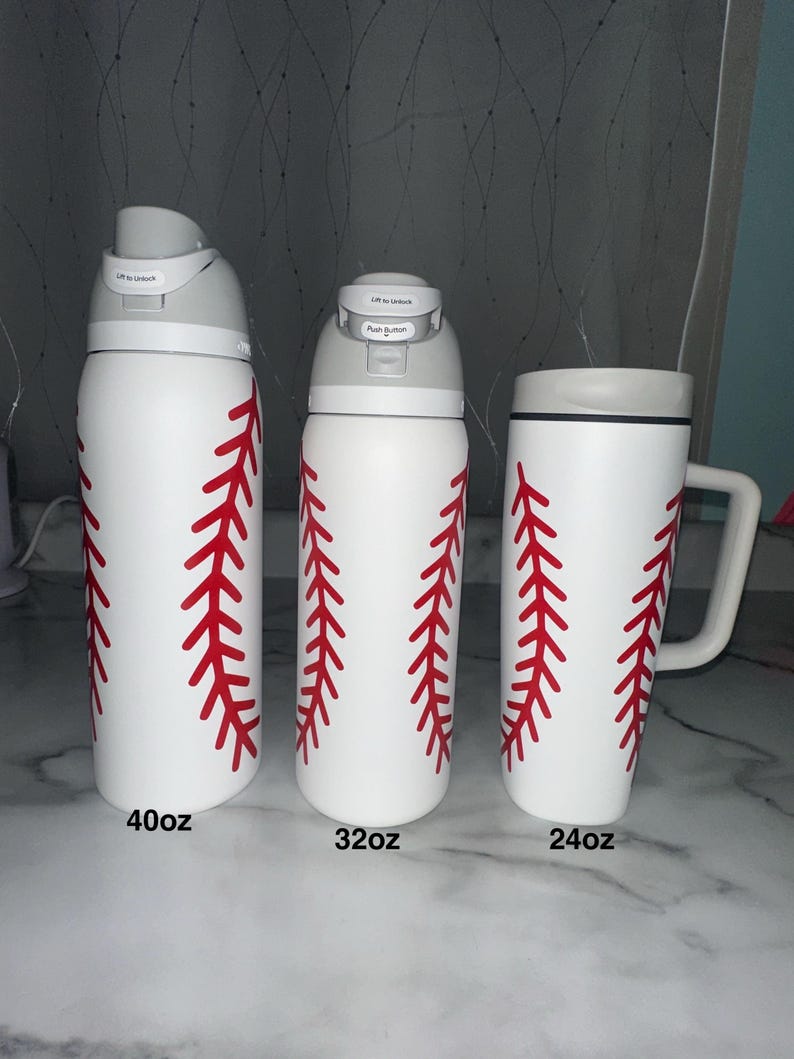 Puede incluir: Tres botellas de agua blancas y una taza con dise&ntilde;os de costuras de b&eacute;isbol rojas. Las botellas est&aacute;n etiquetadas como 40oz y 32oz, y la taza est&aacute; etiquetada como 24oz. Las botellas tienen tapas grises y la taza tiene un borde y asa grises.