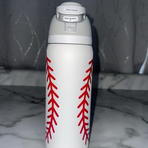 Puede incluir: Botella de agua blanca de 946 ml con dise&ntilde;o de costura de b&eacute;isbol roja. La botella tiene una tapa gris con un bot&oacute;n y las palabras "Lift to Unlock" y "Push Button".