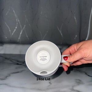 Puede incluir: Una tapa blanca de 24 oz para una taza, con un asa y un mecanismo deslizante a prueba de fugas. La tapa se muestra desde abajo, con el texto "24oz Lid" en la parte inferior. La tapa est&aacute; dise&ntilde;ada para mantener las bebidas seguras y evitar derrames.