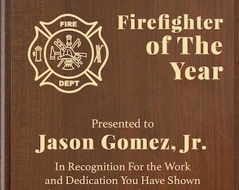 Könnte beinhalten: Holztafel mit goldfarbenem Schriftzug und Feuerwehr-Emblem. Der Text lautet „Feuerwehrmann des Jahres“ und wird Jason Gomez, Jr. überreicht. Die Tafel enthält auch die Lakeshore Fire Department und das Datum Dezember 2022.
