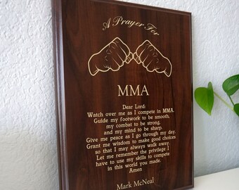 Może przedstawiać: Brązowa drewniana tabliczka z pozłacanymi napisami, na której widnieje napis "A Prayer For MMA". Tabliczka przedstawia stylizowane zdjęcie dwóch splecionych dłoni. Tekst zawiera modlitwę o siłę, przewodnictwo i pokój w zawodach MMA. Tabliczka jest podpisana "Mark McNeal".
