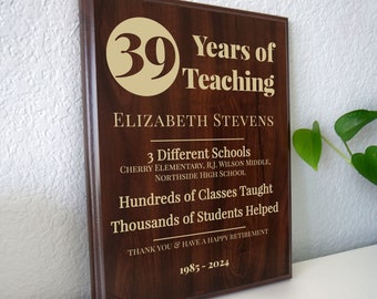 May include: A brown wooden plaque with gold lettering. The plaque reads "39 Years of Teaching", "Elizabeth Stevens", "3 Different Schools", "Cherry Elementary, R.J. Wilson Middle, Northside High School", "Hundreds of Classes Taught", "Thousands of Students Helped", "Thank You & Have a Happy Retirement", and "1985-2024".