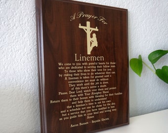 May include: A wooden plaque with a gold inscription that reads "A Prayer For Linemen". The inscription includes a poem about the dedication and risks of linemen. The plaque features a silhouette of a lineman working on a power pole.