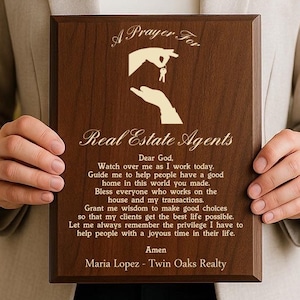 May include: A wooden plaque with a prayer for real estate agents. The plaque is brown with gold lettering and a graphic of a hand holding a key. The text includes the name Maria Lopez and Twin Oaks Realty.