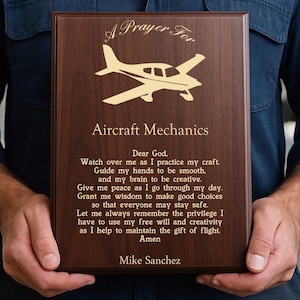 Può includere: Targa in legno marrone con la scritta "A Prayer For Aircraft Mechanics" e un'illustrazione di aereo dorata. La targa include anche una preghiera e il nome "Mike Sanchez".