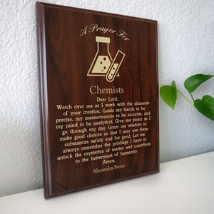 May include: A dark brown wooden plaque with engraved text and a graphic of laboratory equipment. The text reads "A Prayer For Chemists" and includes a prayer. A decorative item for chemists.