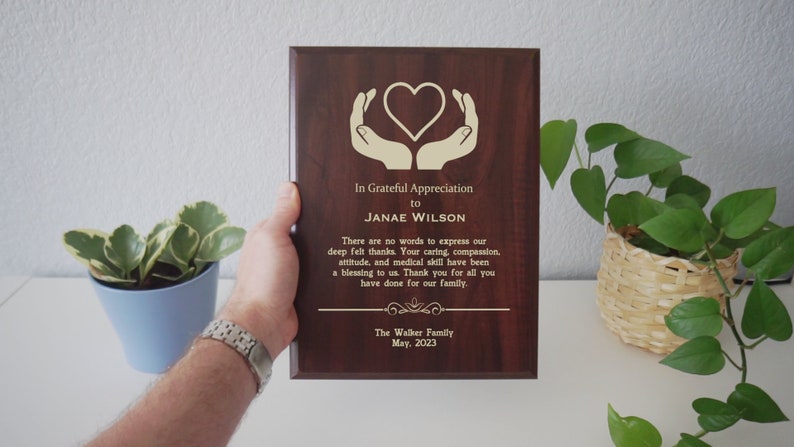 May include: A dark brown wooden plaque with a gold heart and hands design. The plaque says "In Grateful Appreciation to JANAE WILSON. There are no words to express our deep felt thanks. Your caring, compassion, attitude, and medical skill have been a blessing to us. Thank you for all you have done for our family. The Walker Family May. 2023."