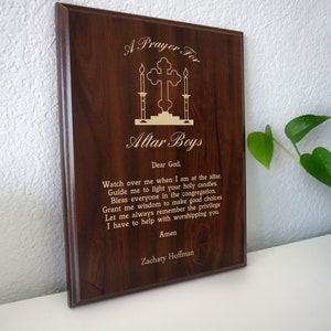 May include: A wooden plaque with a prayer for altar boys. The plaque is brown with gold lettering and a gold cross with candles. The text reads: "A Prayer For Altar Boys Dear God. Watch over me when I am at the altar. Guide me to light your holy candles Bless everyone in the congregation Grant me wisdom to make good choices Let me always remember the privilege I have to help with worshipping you Amen Zachary Hoffman"