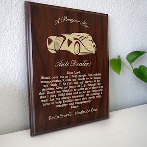 May include: A dark brown wooden plaque with an engraved classic car design and text. The text reads "A Prayer For Auto Dealers" and a prayer. The plaque is displayed on a white surface.