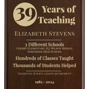 May include: A brown plaque with gold lettering celebrating 39 years of teaching. The plaque reads "Years of Teaching", "Elizabeth Stevens", "3 Different Schools", "Cherry Elementary, R.J. Wilson Middle, Northside High School", "Hundreds of Classes Taught", "Thousands of Students Helped", "Thank You & Have a Happy Retirement", and "1985-2024".
